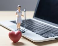 A woman in a white t shirt is holding up a stethoscope in front of a laptop, health and medical stock image