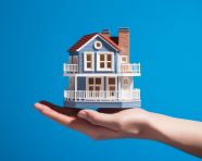 A hand holding a house with a blue background, home loan stock image