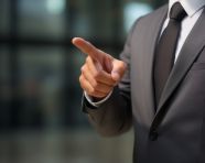 Businessman in business suit with finger up pointing at something with finger down on grey
