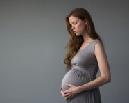 Happy pregnant woman holds her belly on gray background, pregnant women pictures, maternity photos