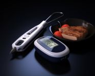 A digital glucometer is placed in front of a dark background, diabetes concept
