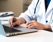 A male doctor writing on a sheet of paper working on her laptop, medical images stock