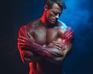 A muscular man with folded hands is standing