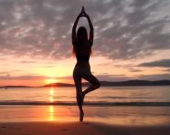 Woman practicing yoga at beach sunset