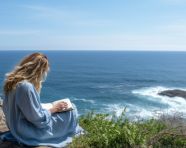 A woman sits on a cliff overlooking the ocean writing in a journal