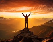 A person stands on a mountaintop looking out at the view